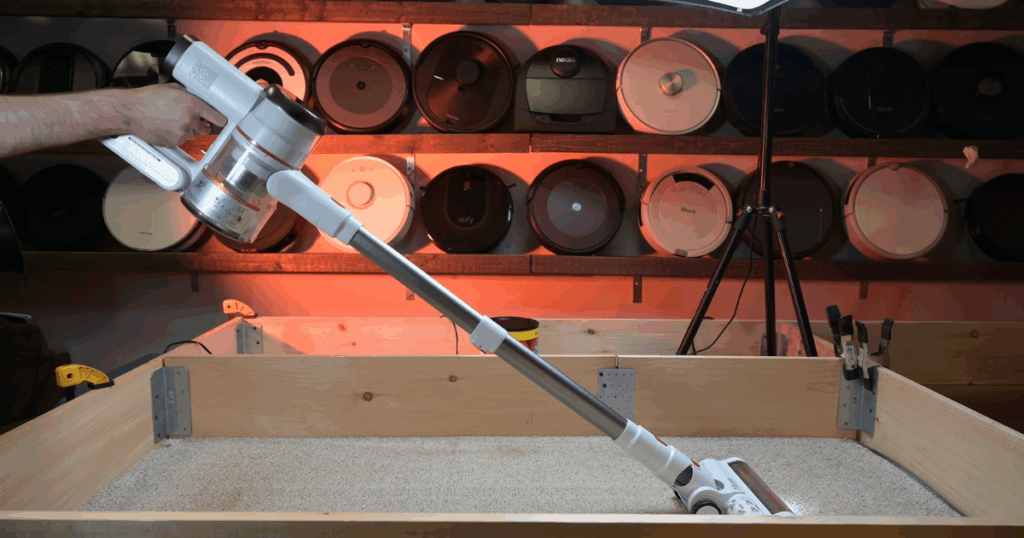 Tikom V500 cordless vacuum being tested on carpet in a wooden testing box at Vacuum Wars studio.