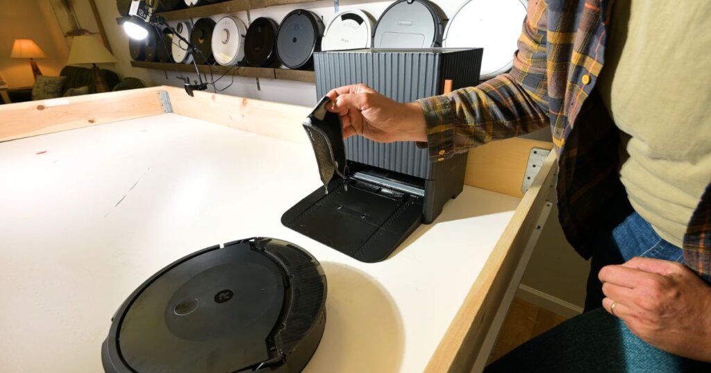 A hand removes a dirty mop pad from the Roomba Combo 10 Max dock during a test surrounded by other robot vacuums.