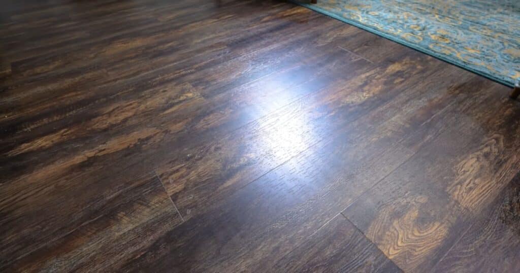 Hardwood floor with visible streak lines left after mopping, adjacent to a patterned area rug.
