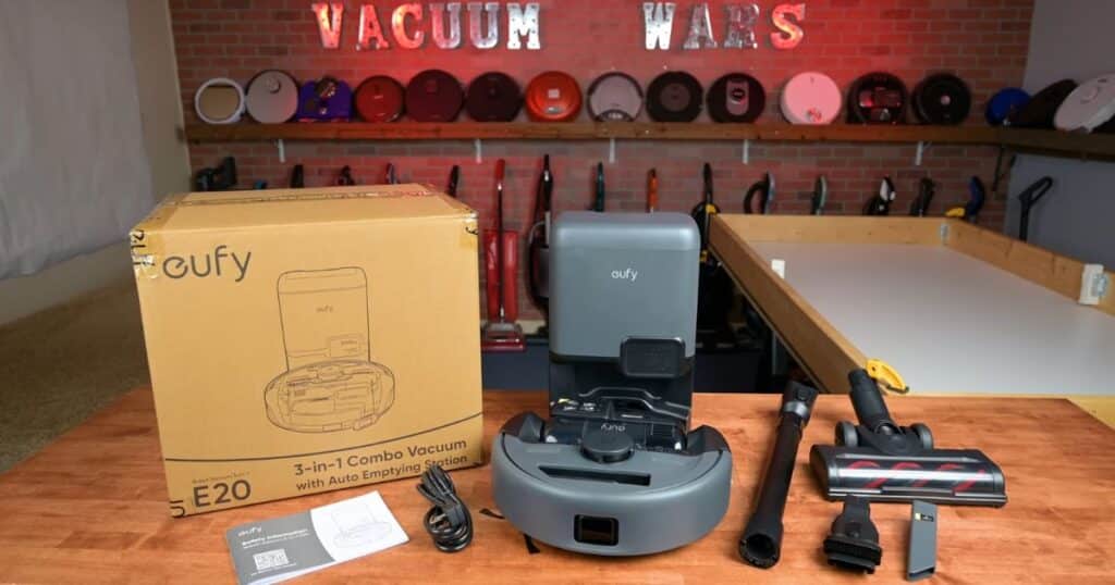 Eufy E20 3-in-1 robot vacuum with auto-empty base, box, and included cordless attachments shown on a table.