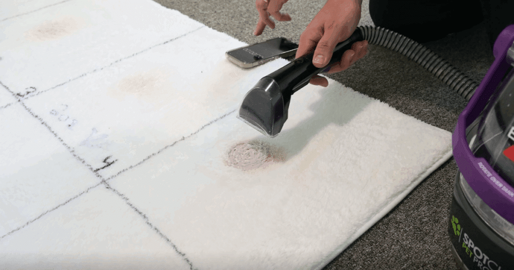 Spot cleaner in use, spraying cleaning solution onto a carpet stain before scrubbing and extracting dirty water.