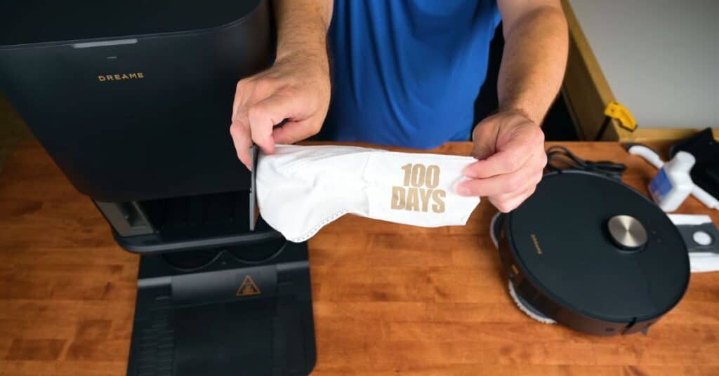 Person holding disposable dust bag labeled “100 Days” next to Dreame L50 Ultra dock.