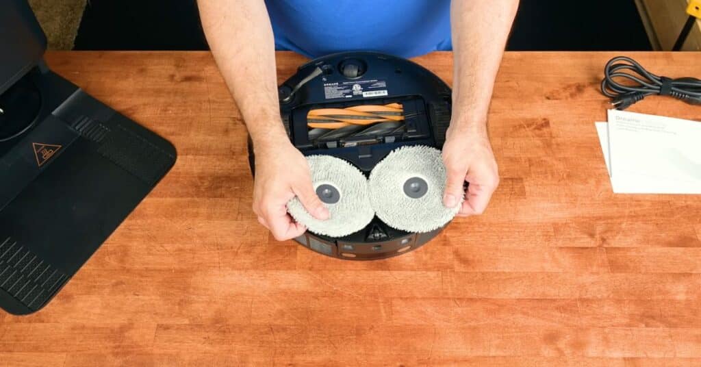 Person holding two circular mop pads on the underside of the Dreame L50 Ultra robot vacuum.
