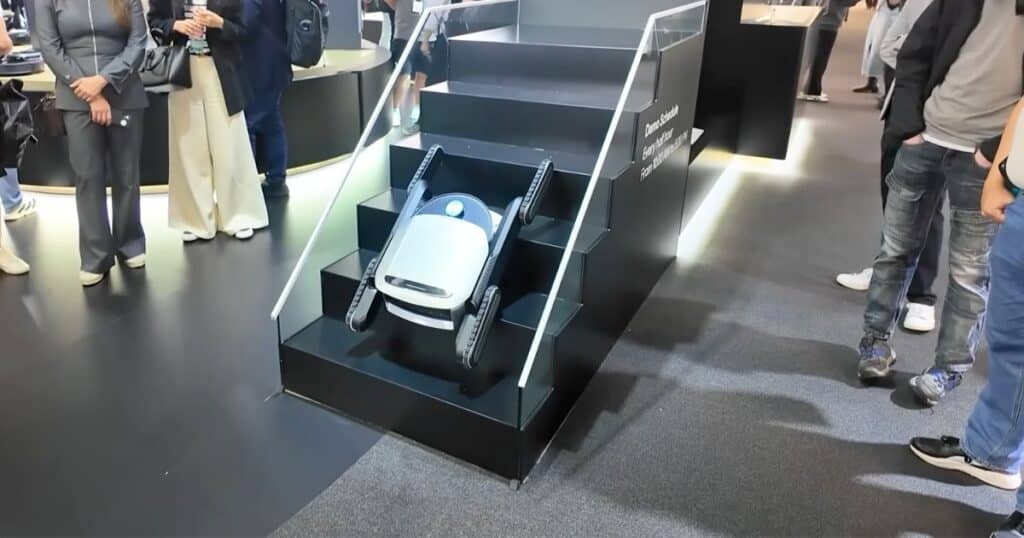 Dreame stair-climbing robot vacuum demonstrated at IFA 2025, shown midway up a black staircase with rubber tracks extended.
