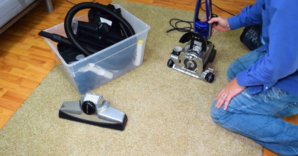 Plastic bin with Kirby vacuum attachments, Kirby Avalir vacuum on carpet, and detached floorhead shown.