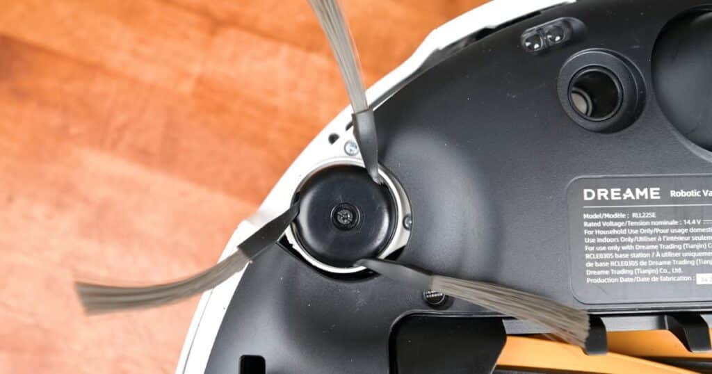 Close-up of the underside of a Dreame robot vacuum showing the three-armed side brush installed near the edge, designed to sweep debris into the cleaning path.