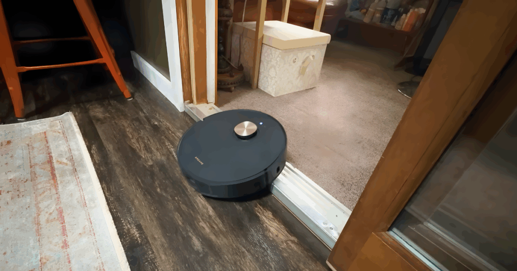 Dreame L50 threshold climbing | Vacuum Wars A robot vacuum (Dreame L50) attempting to cross a tiered doorway threshold between two flooring types. The image illustrates the kind of stepped or double-threshold obstacle that challenges many robot vacuums