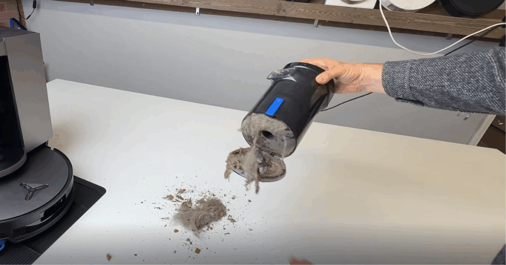A person emptying the Ecovacs Deebot X11 OmniCyclone’s bagless dustbin, showing damp debris buildup caused by simultaneous vacuuming and mopping.