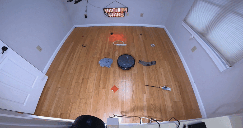 Ecovacs Deebot X11 OmniCyclone robot vacuum performing an obstacle avoidance test at the Vacuum Wars studio, navigating around common household objects on hardwood flooring.