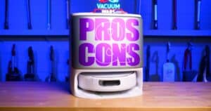 Front view of the Narwal Flow robot vacuum inside its docking station with bold “Pros Cons” text displayed across the front, photographed in a blue-lit studio.