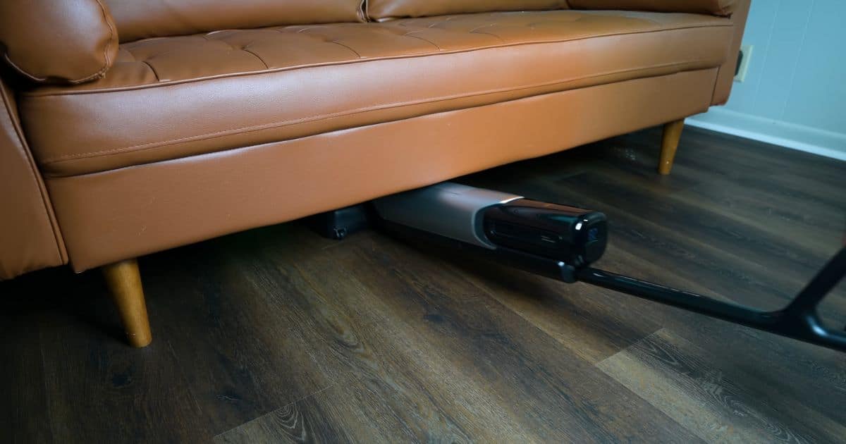A hard floor cleaner laid nearly flat to reach underneath a sofa, cleaning the floor in a low, narrow space.
