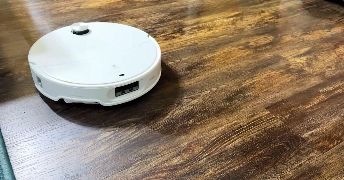 Roborock QRevo CurvX robot vacuum mop moving across a dark, wood-look hard floor that appears evenly cleaned with no visible streaks.