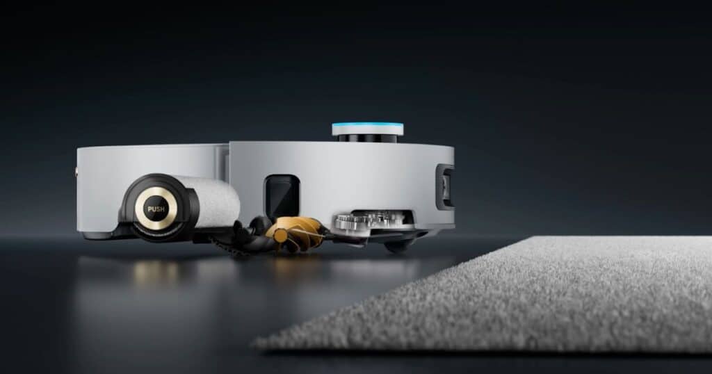 | Vacuum Wars Side view of the Dreame Aqua 10 Ultra Roller robot vacuum approaching a carpeted surface, illustrating the Auto-Seal Carpet Protection system that deploys a guard to shield the mop roller when detecting carpet, preventing moisture transfer during cleaning.