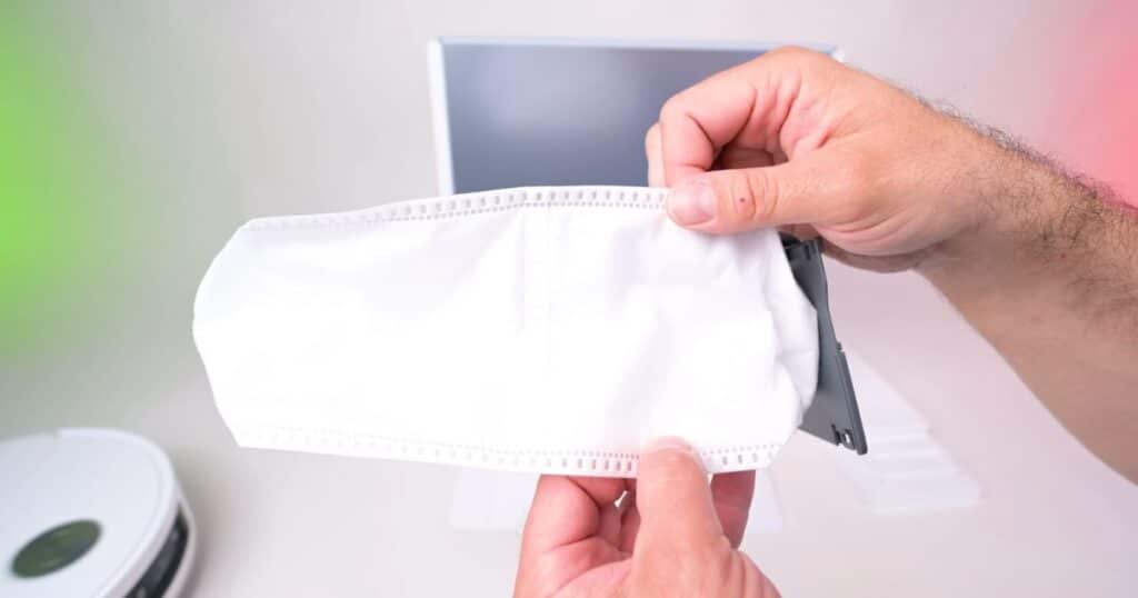 | Vacuum Wars Close-up of a person holding the Dreame Aqua 10 Ultra Roller’s disposable 3-liter dust collection bag, which attaches inside the self-emptying dock for debris storage lasting up to approximately 100 days depending on cleaning frequency.