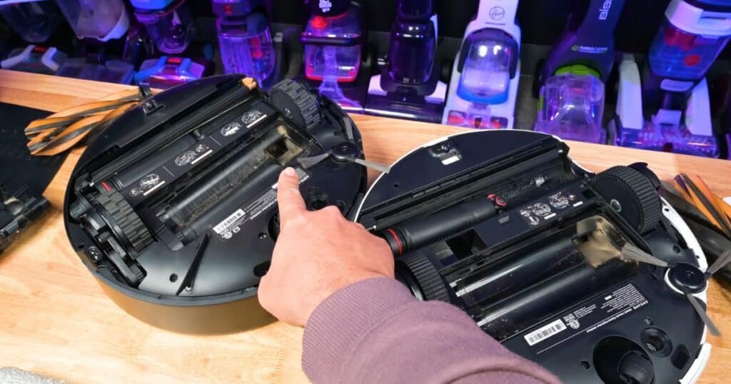 Close-up of the MOVA Z60 and Dreame Aqua10 robot vacuums turned upside down as a person points to the intake channel of the Z60.
