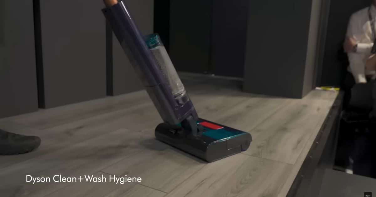 | Vacuum Wars Dyson Clean+Wash Hygiene wet floor cleaner shown on a light wood floor, with on-screen text reading “Dyson Clean+Wash Hygiene”.