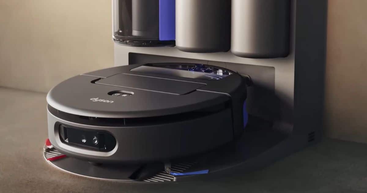 | Vacuum Wars Dyson Spot+Scrub Ai robot vacuum positioned at its docking station, with the robot partially aligned under the dock’s housing.