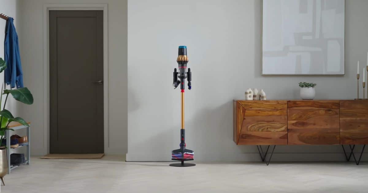 | Vacuum Wars The Dyson V16 Piston Animal cordless vacuum is standing upright in the middle of a living room, with a red-and-blue floor head on a light-colored floor.