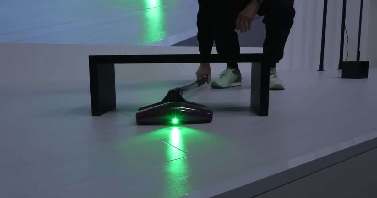 | Vacuum Wars The low-profile Dyson PencilVac vacuum head reaches under a table while projecting a bright green light on a hard floor.