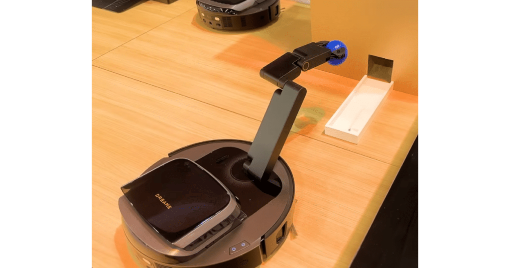 Dreame Cyber 10 Ultra at CES 2026 | Vacuum Wars Dreame Cyber 10 Ultra robot vacuum with an extended robotic arm lifting a small object during a CES demonstration.