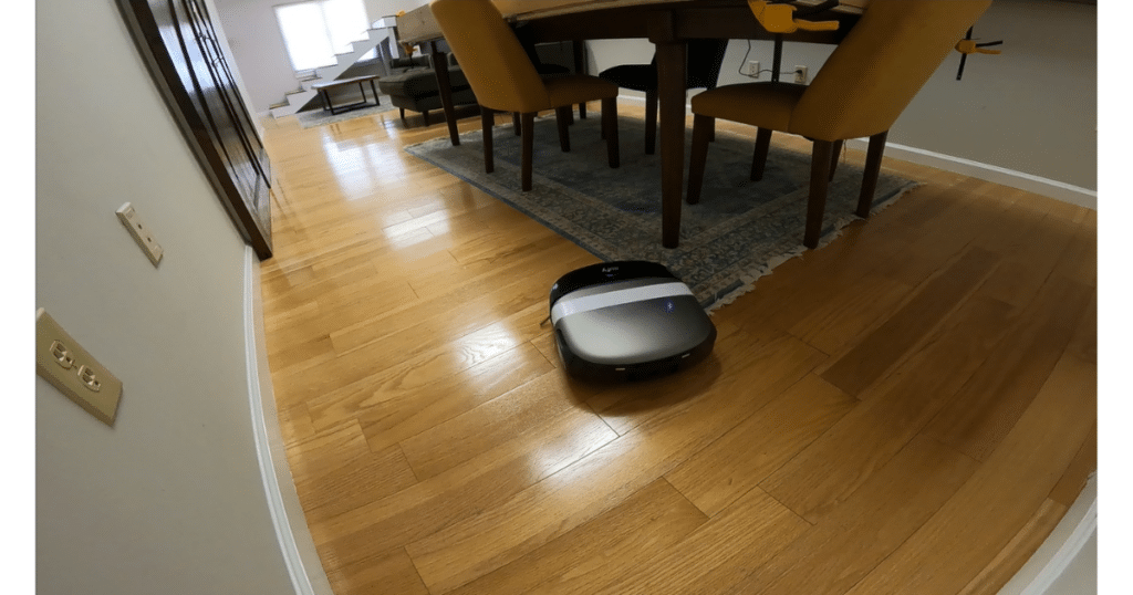 Eufy Omni S2 Robot Vacuum Navigating a Room at Vacuum Wars | Vacuum Wars Eufy Omni S2 robot vacuum navigating across hardwood flooring near a dining area in a mixed-floor home environment.