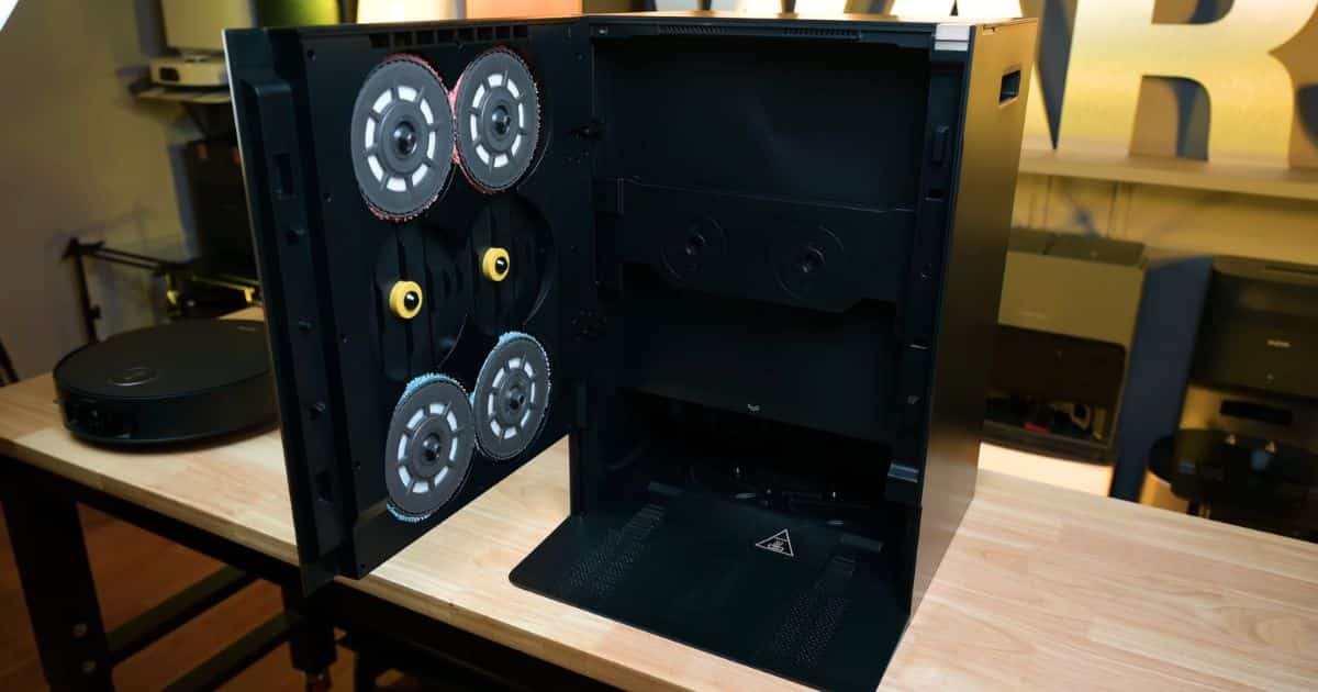 | Vacuum Wars The Mobius 60 dock with its front panel opened, revealing circular mop pad holders and internal compartments; the robot vacuum sits on the table nearby.