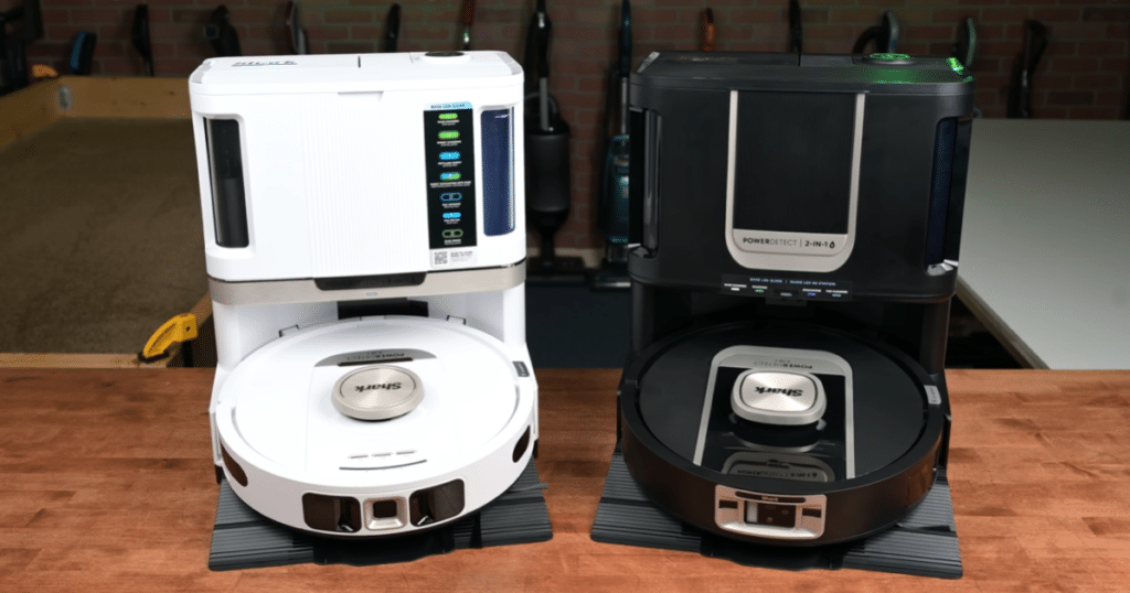 Shark PowerDetect NeverTouch vs PowerDetect ThermaCharged NeverTouch | Vacuum Wars Side-by-side photo of the Shark PowerDetect ThermaCharged NeverTouch Pro in white and the Shark PowerDetect NeverTouch Pro in black, each docked on their auto-empty bases on a workbench.