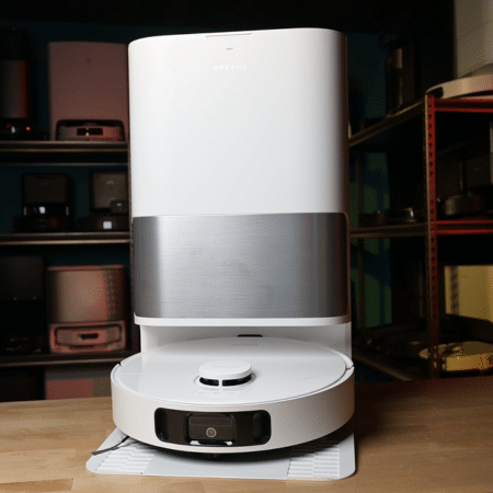 Dreame D30 Ultra in studio 450 ©Vacuum Wars | Vacuum Wars Tall white and gray robotic device on a wooden workbench with shelves in the background.