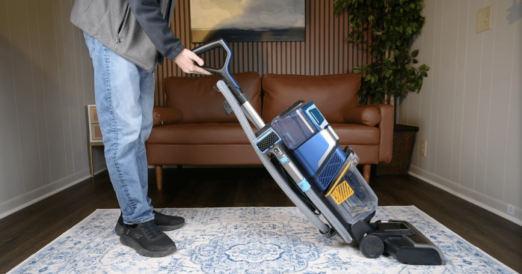 Shark CarpetXpert EX301 at Home | Vacuum Wars Person using the Shark EX301 CarpetXpert carpet cleaner on an area rug in a living room, demonstrating its upright design and PowerSpray cleaning system.