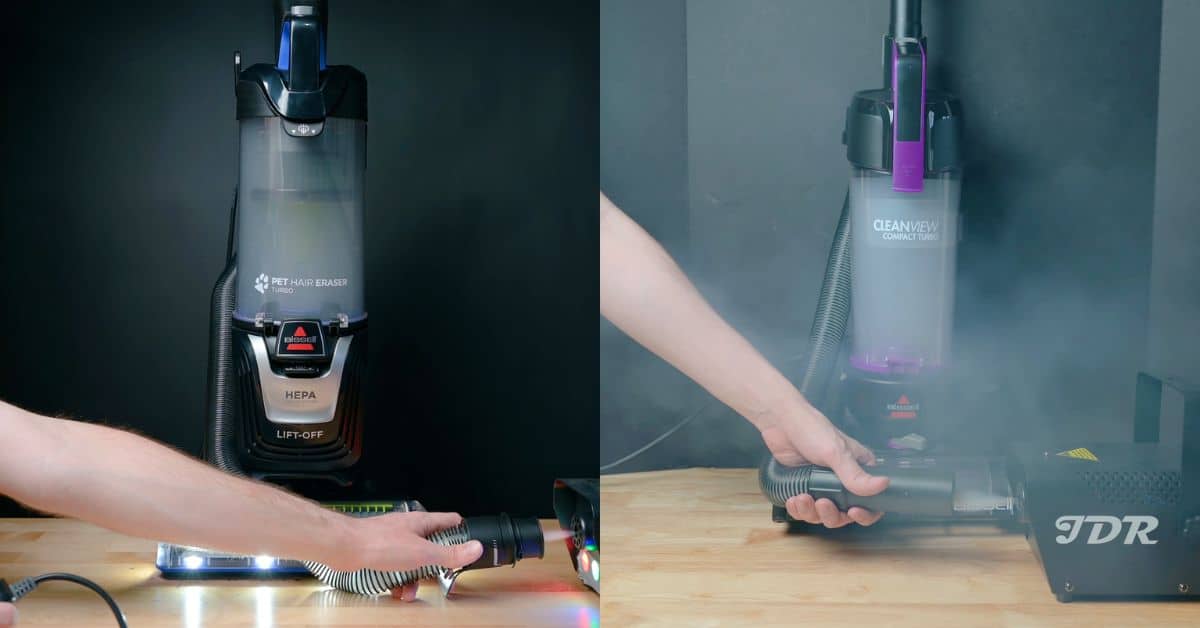 | Vacuum Wars Side-by-side filtration test image showing a Bissell Pet Hair Eraser Turbo upright on the left and a Bissell CleanView Compact Turbo on the right. There's visible dust or smoke escaping around the CleanView Compact Turbo as a hand holds the hose near a JDR test machine—from our best cheap upright vacuum review and comparison.