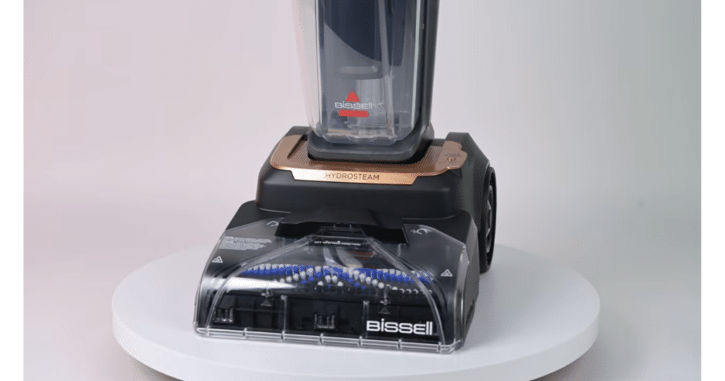 Bissell HydroSteam 4123 in Vacuum Wars Studio | Vacuum Wars Front view of the Bissell Revolution HydroSteam 4123 carpet cleaner on a white surface, showing its clear cleaning head and water tank.