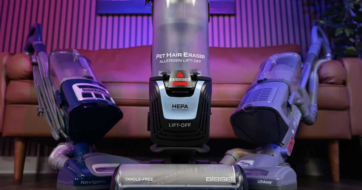 | Vacuum Wars Bissell Pet Hair Eraser Allergen Lift-Off 39883 upright vacuum centered between two Shark Navigator Lift-Away vacuums, with visible labels for HEPA sealed system, Lift-Off, and tangle-free brush roll.