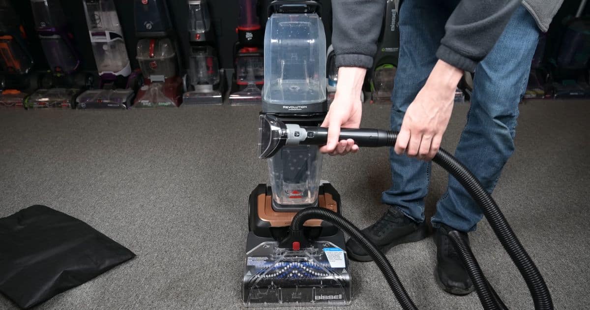 | Vacuum Wars Person using the Bissell HydroSteam hose attachment while the machine stands upright on carpet in a test room.