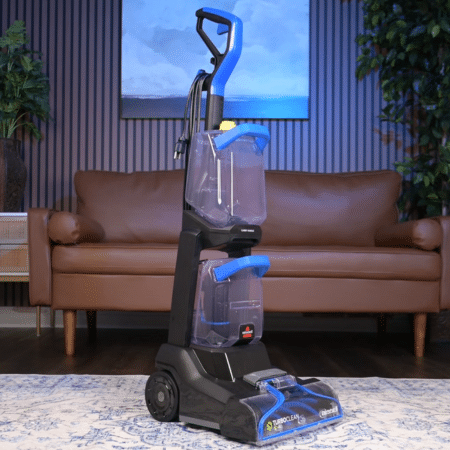 Bissell TurboClean Pet XL in studio 450 ©Vacuum Wars | Vacuum Wars Upright blue-and-black floor scrubber on a rug in a living room, ready for use near a brown sofa.