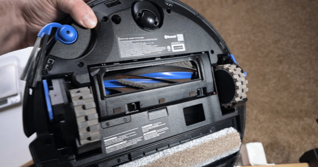 Ecovacs T90 Pro Omni Robot Vacuum Hair Tangle Test | Vacuum Wars Inside view of a robotic vacuum cleaner with its brush roll exposed as a hand lifts the back panel.