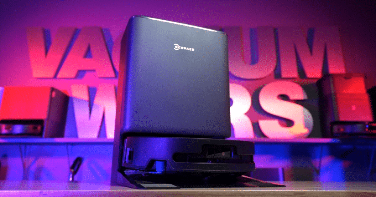 Blue compact speaker perched on a docking base in a neon-lit studio with large pink letters in the background.
