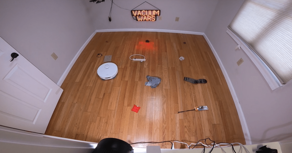 MOVA P10 Pro Ultra Obstacle Avoidance | Vacuum Wars MOVA P10 Pro Ultra robot vacuum navigating a hardwood floor test area with scattered household objects for obstacle avoidance evaluation.