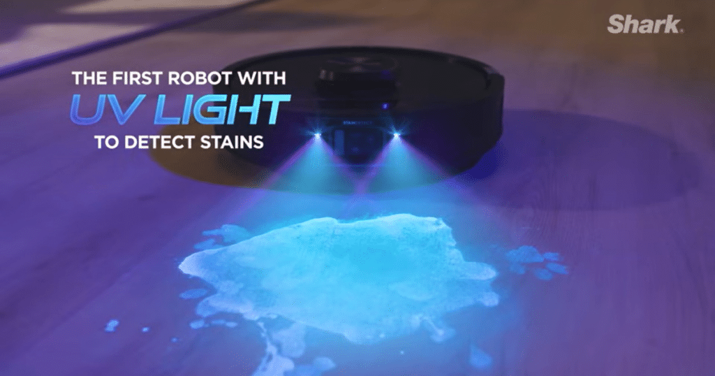 Shark Powerdetect UV Reveal light reveal | Vacuum Wars Shark robot vacuum using UV light to detect stains on hard floor, highlighting spill for targeted cleaning.