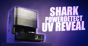 Shark Powerdetect UV Reveal title | Vacuum Wars Promotional image showing a black UV detection device on a pedestal with purple glow and bold text: 'SHARK POWERDETECT UV REVEAL' on the wall to the right
