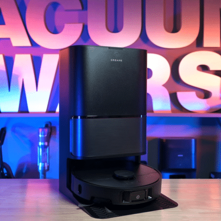 Dreame L40 Ultra in studio 450 | Vacuum Wars Two-part black appliance (tall unit with base) on a wooden surface, with a round robot vacuum in front and bold neon letters in the background