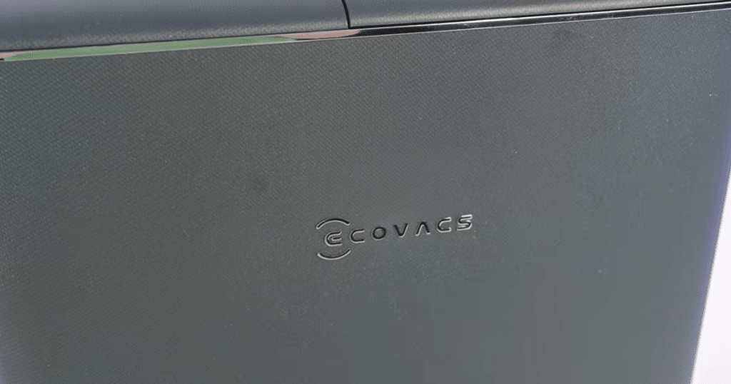 Ecovacs Deebot T90 Pro Omni Surface Texture | Vacuum Wars Close-up of the textured outer shell on an Ecovacs robot vacuum docking station, featuring the embossed Ecovacs logo in the center.