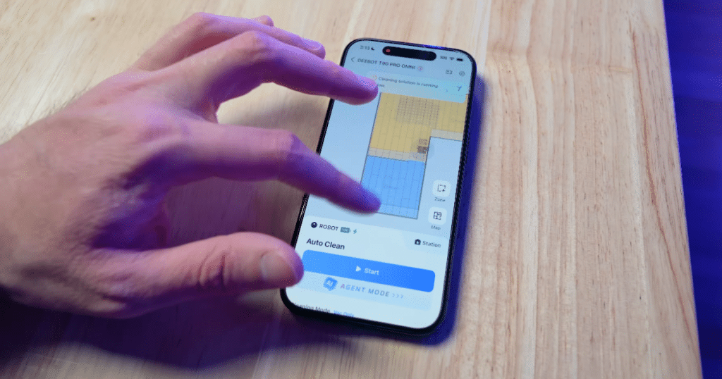 Ecovacs T90 App | Vacuum Wars A person using the Ecovacs mobile app on a smartphone to customize cleaning settings and room mapping for the Deebot T90 Pro Omni robot vacuum.