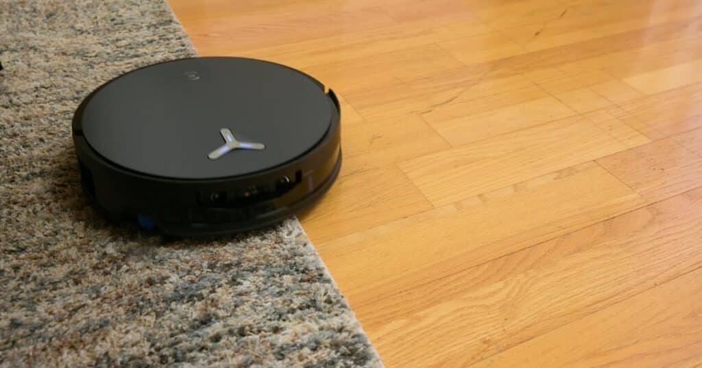 | Vacuum Wars Ecovacs X12 OmniCyclone robot vacuum moving from carpet onto a hard floor in a home setting.