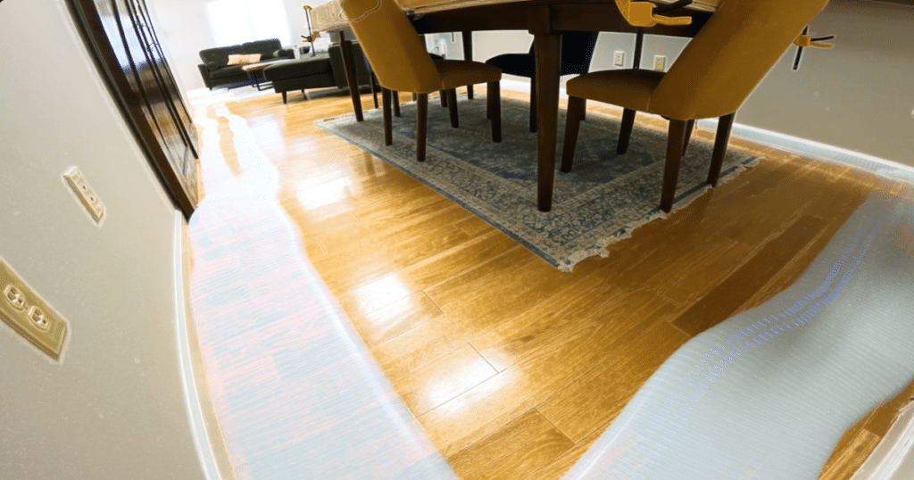 Eufy C28 Navigation 1 | Vacuum Wars Dining room with a dark wood table and yellow chairs on a blue patterned rug; showing the Eufy C28 robot vacuum begin to navigation around the room.