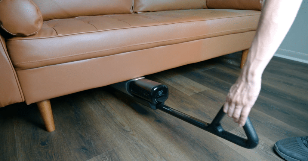 MOVA X4 Lay Flat Design | Vacuum Wars The MOVA X4 Pro cordless floor cleaner is shown lying flat to clean underneath a low-profile couch on a hardwood floor.