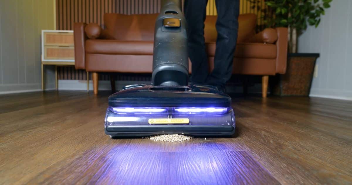 | Vacuum Wars Roborock F25 Ultra vacuum mop picking up a small pile of dry debris on a hard floor, with LED lights illuminating the cleaning path.