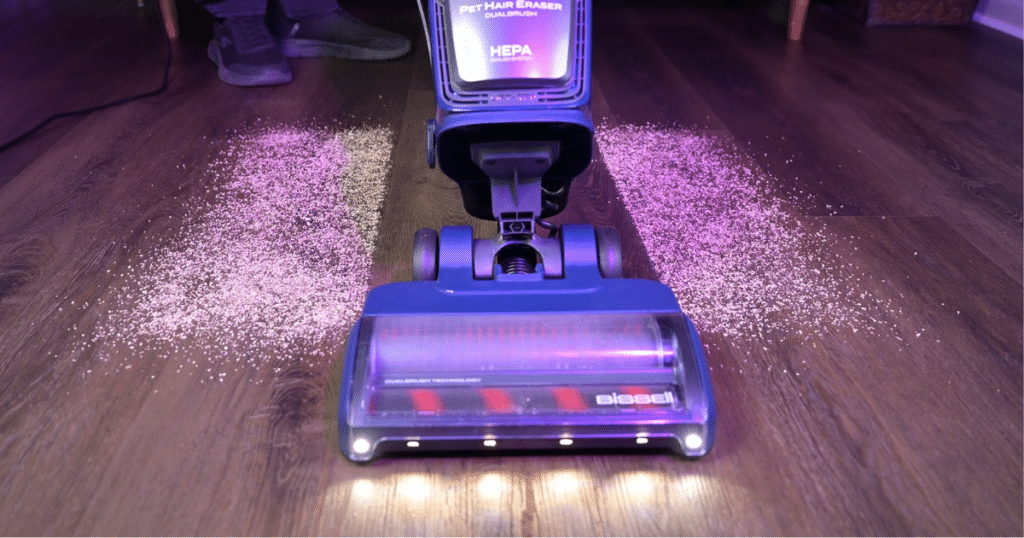Bissell Pet Hair Eraser DualBrush 42943 vacuum cleaning debris on a hard floor during Vacuum Wars testing, highlighting its dual-brushroll floorhead and LED headlights.