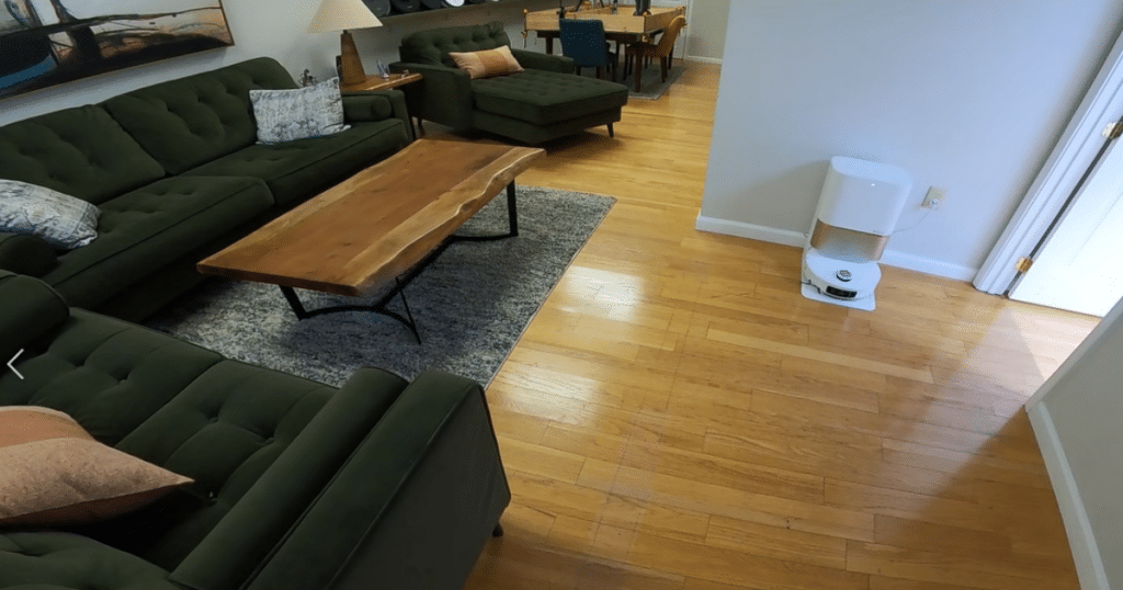 Dreame L60 Pro Ultra robot vacuum and multifunction dock cleaning a mixed hard floor and carpet living room with dual spinning mop pads, heated-water mopping, and automatic mop lifting
