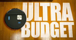 MAMNV D13S Max Review Vacuum Wars | Vacuum Wars Robotic vacuum cleaner on a wooden floor beside oversized white letters reading ULTRA BUDGET.