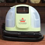Bissell Little Green Mini Cordless 150 | Vacuum Wars Compact upright carpet cleaner with a light green and white body and black hose, on a wooden floor.